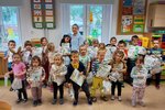 Grupa dzieci z nauczycielem stoją na tle okna. W ręku trzymają dyplomy i nagrody.